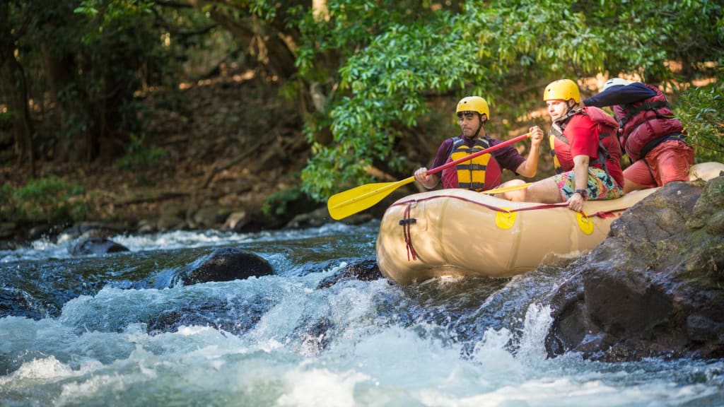 Two people in helmets and life vests paddle an inflatable raft on a rocky river surrounded by dense greenery—perfect for adventure seekers who know what to pack for Costa Rica's wild landscapes.